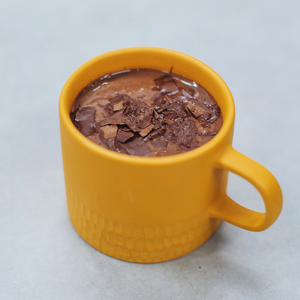 A yellow mug with hot chcolcoate and chocolate flakes sprinkled on the top. 