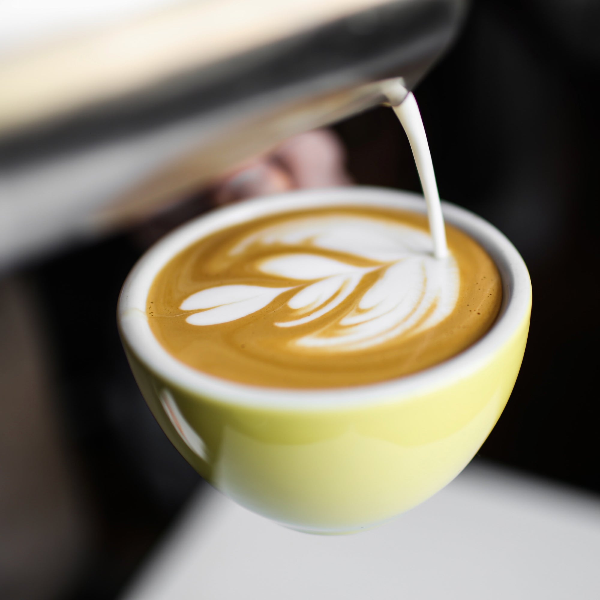 pouring latte art into a yellow coffee cup
